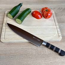 Das F. Dick 1905 Kochmesser liegt auf einem Schneidebrett mit Gurken und Tomaten. Die markanten Metallringe im Griff sind gut sichtbar.