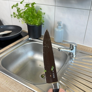 Das F.-Dick-1905-Messer wird mit Kräuterresten über das Spülbecken gehalten. Die Klinge ist noch verschmutzt.