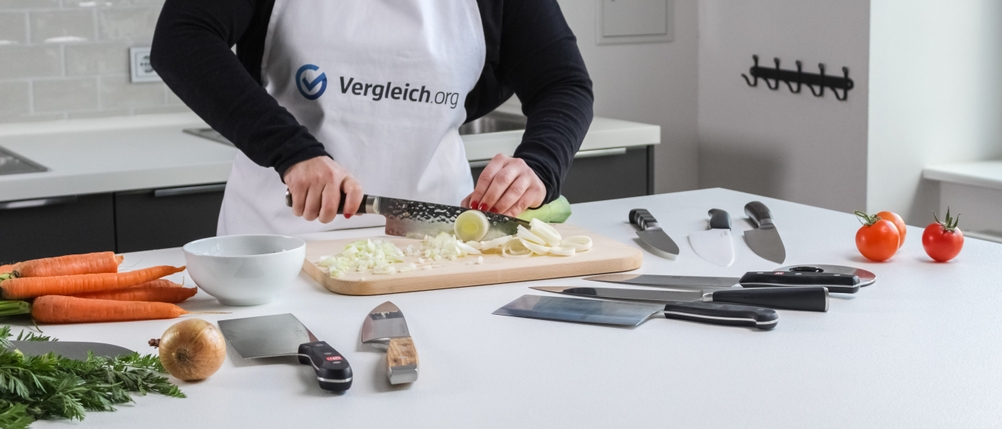 Gemüse wird auf einem Schneidebrett mit einem Kochmesser klein geschnitten.