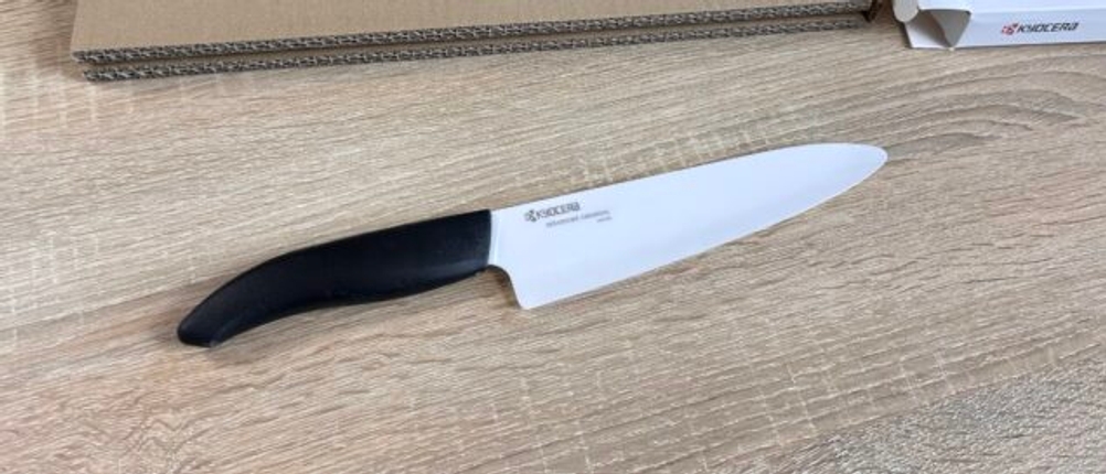 Das Kyocera-Keramikmesser liegt ausgepackt auf dem Tisch. Daneben liegt die geöffnete Verpackung mit Kartoneinlage.