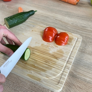 Das Kyocera-Keramikmesser wird beim Schneiden einer Gurke angesetzt. Zwei Tomaten liegen auf dem Brett.