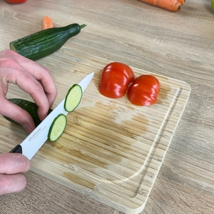 Das Kyocera-Keramikmesser schneidet eine Gurke auf einem Holzbrett. Die Hand führt den Schnitt präzise aus.