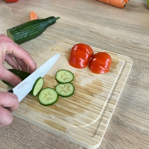 Mehrere Gurkenscheiben liegen auf dem Brett, geschnitten mit dem Kyocera-Keramikmesser. Die Hand führt den letzten Schnitt aus.