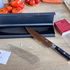 Das Shan-Zu-Kochmesser liegt ausgepackt neben geöffneter Verpackung, Anleitung und Klingenschutz. Die Damaststruktur der Klinge ist gut erkennbar.