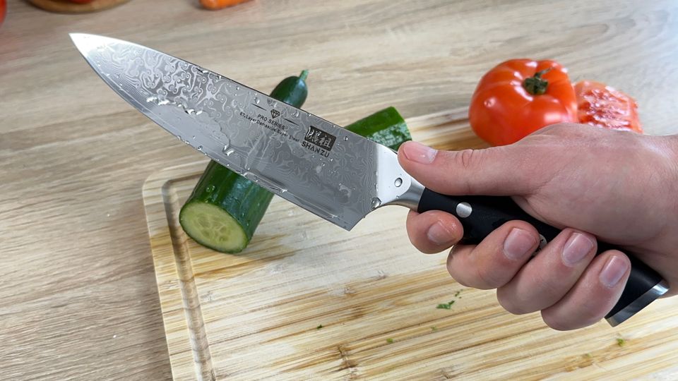 Das Shan Zu Kochmesser wird nach dem Schneiden mit feuchter Klinge in der Hand gehalten. Wasserperlen sind sichtbar.