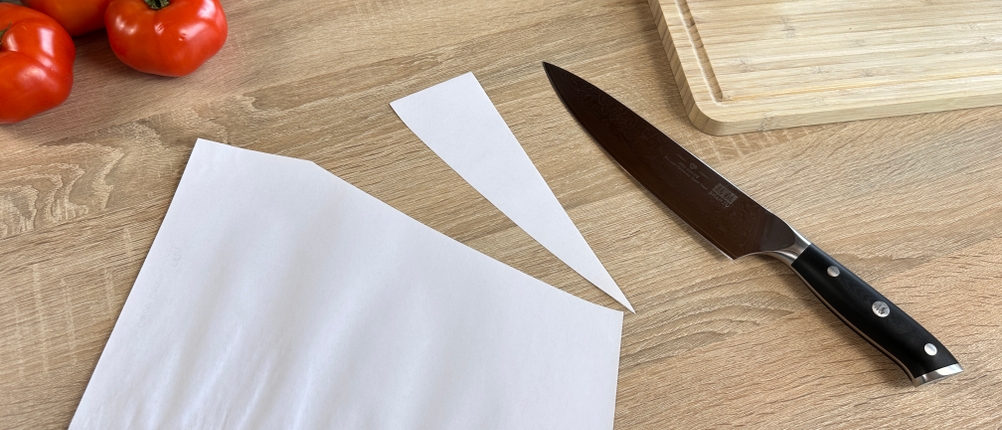 Das Shan-Zu-Kochmesser liegt neben einem sauber geschnittenen Papierbogen auf dem Tisch. Gemüse ist im Hintergrund sichtbar.