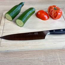 Das Shan Zu Kochmesser liegt auf einem Schneidebrett mit Gurken und Tomaten. Die dunkle Klinge zeigt ein feines Damastmuster.