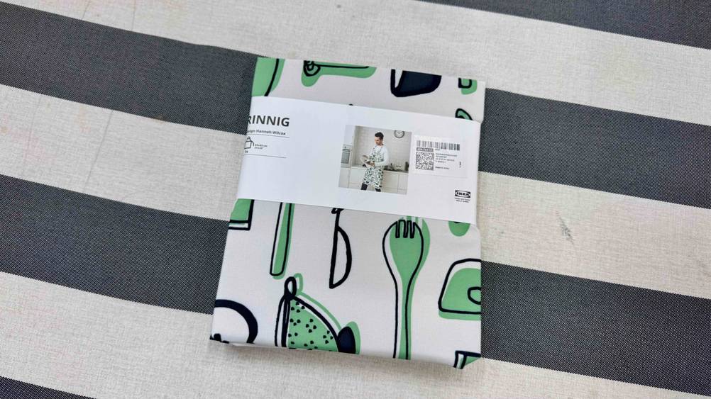 Kochschürze getestet: Die verpackte Schürze auf einem gestreiften Stoff.
