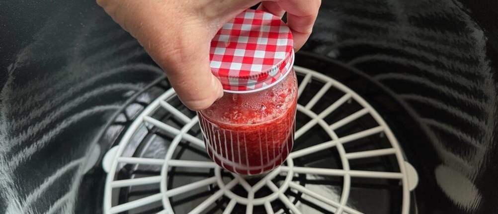 Eine Hand stellt ein Einmachglas in den Behälter des Kochstar-99102035-Einkochautomat 