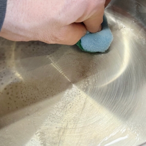 Eine Person reinigt den getesteten Kochtopf von WMF mit einem Schwamm.