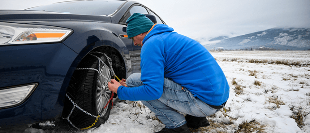 König-Schneeketten im Test: Ein Mann montiert Schneeketten am Auto.