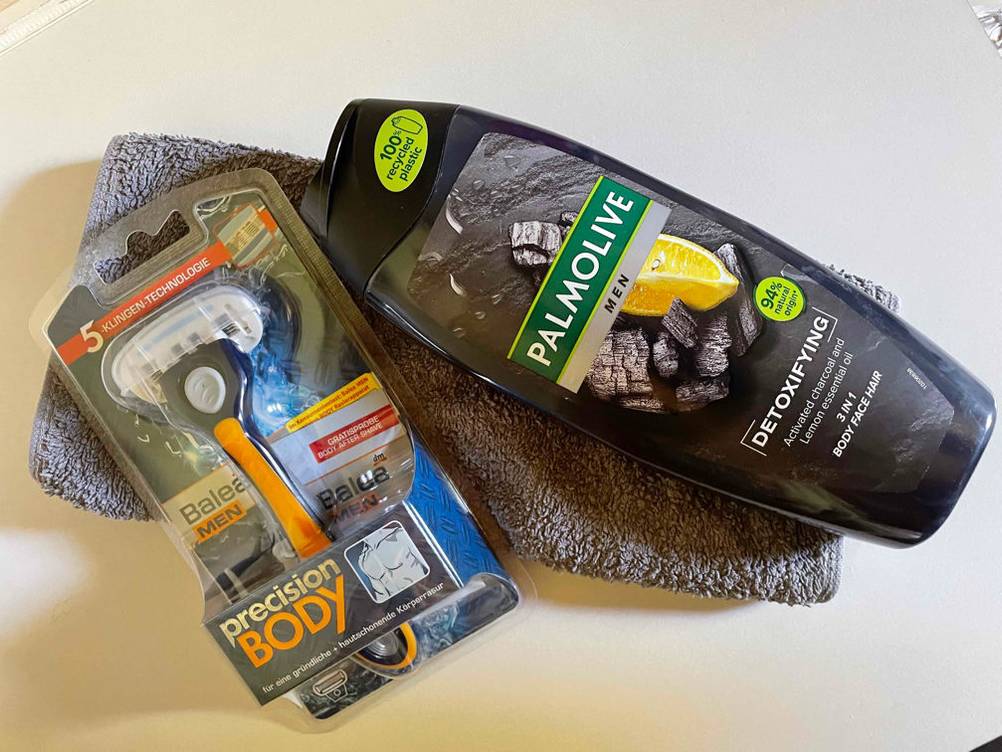 Ein getesteter Körperrasierer liegt verpackt mit einem Duschgel auf einem Handtuch.