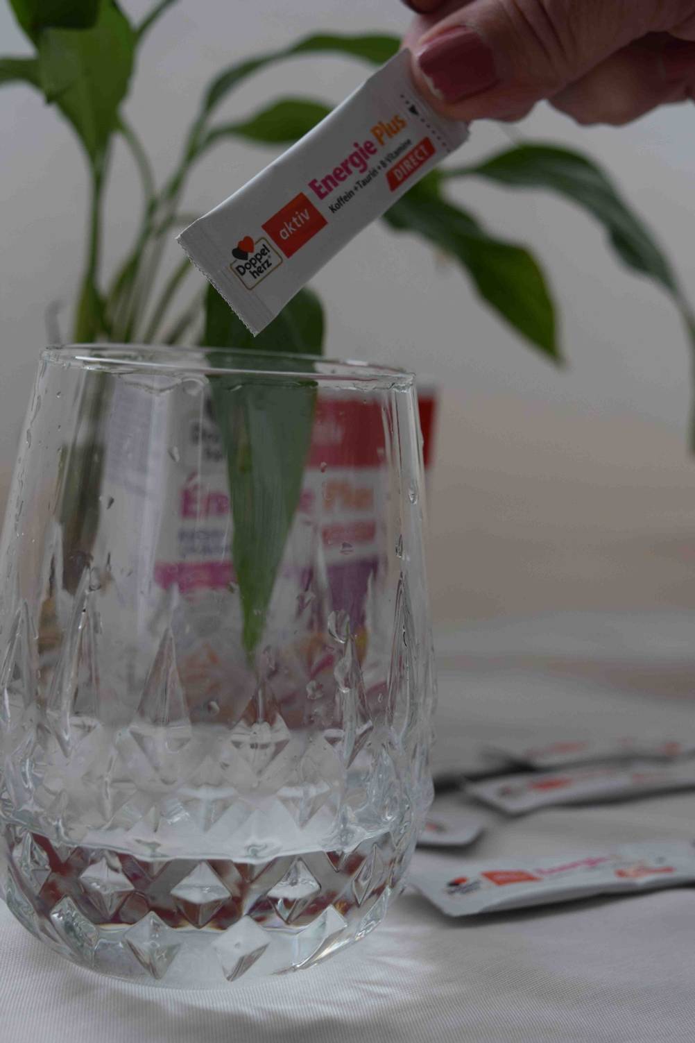 Koffeintabletten getestet: Eine Hand hält ein Päckchen über ein Glas mit Wasser.