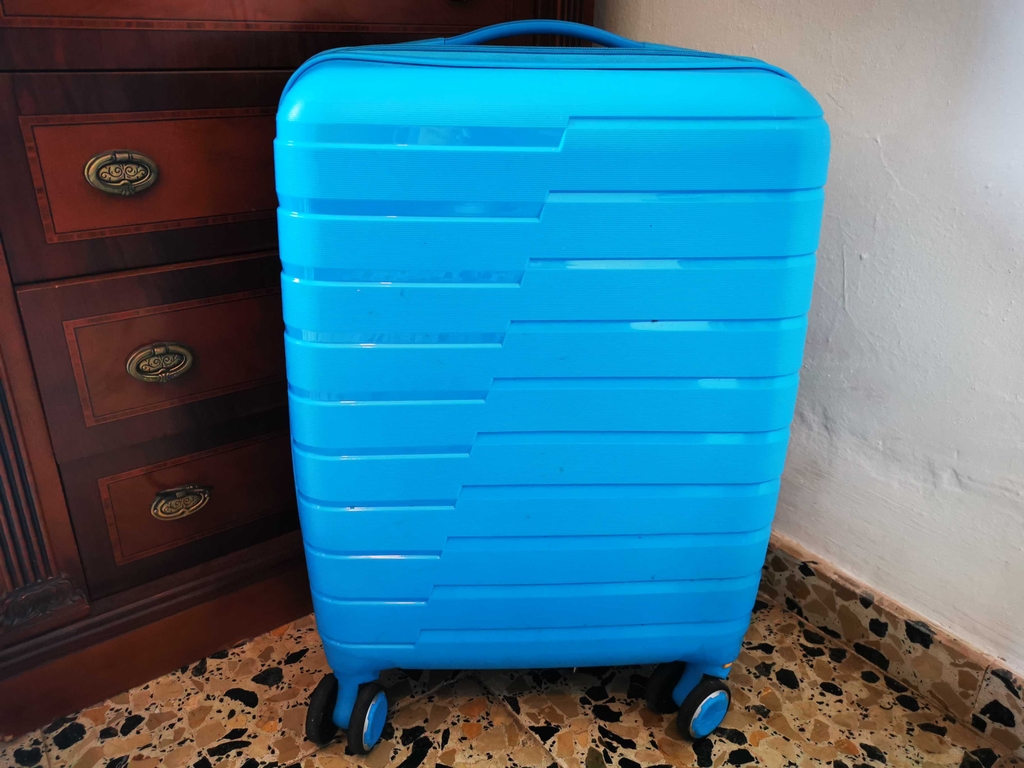Der türkisfarbene, getestete Koffer steht auf dem Boden.
