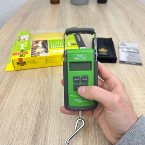 Eine Burg-Wächter-Tara-PS-7600-Kofferwaage wird von einer Hand gehalten, während der Metallhaken frei nach unten zeigt.