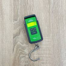 Eine Burg-Wächter-Tara-PS-7600-Kofferwaage liegt mit grünem Gehäuse und Metallhaken einsatzbereit auf einem Tisch.