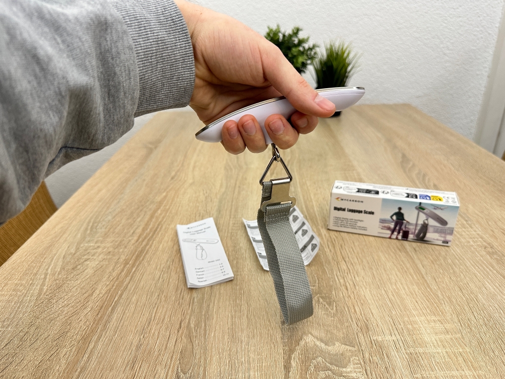 Eine Mycarbon-DS2-Kofferwaage wird von einer Hand gehalten, während das Trageband nach unten hängt.