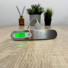 Eine Mycarbon-DS2-Kofferwaage steht eingeschaltet auf einem Tisch, während das grün beleuchtete Display den Messwert anzeigt.