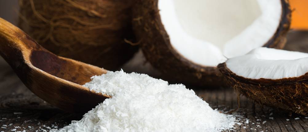 Kokosraspeln mit einem Holzlöffel vor Kokosnüssen