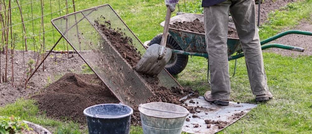 Kompostsieb im Garten getestet: Szene in einem Garten, in der ein Mann aus einer Schubkarre Kompost auf ein Gartensieb gibt.
