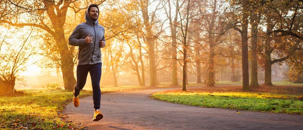 Kompressions-Laufhose Herren im Test: Ein Mann in langer Hose joggt durch den herbstlichen Sonnenaufgang.