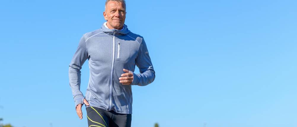 Kompressions-Laufhose Herren im Test: Ein Mann joggt unter blauem Himmel.