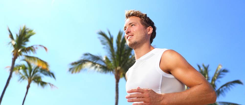 Kompressionsshirt-Herren-Test: Mann joggt in weißem Funktionsshirt unter Palmen