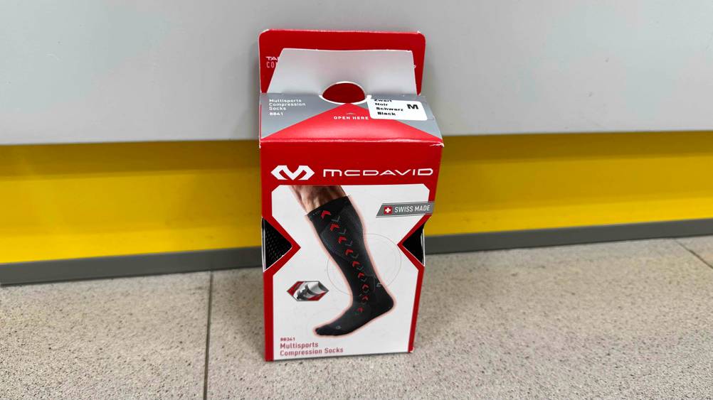 Vor einer hellen Wand auf dem Boden stehen die getestesten Kompressionsstrümpfe in der Verpackung.