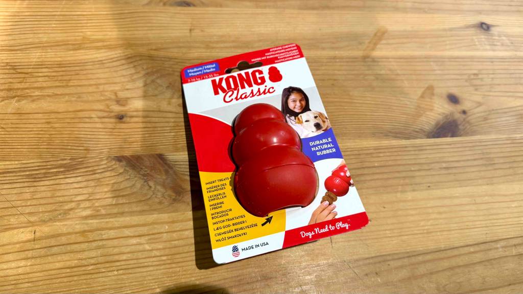 Ein robustes Hundespielzeug im Kartonblister liegt zum testen auf einer Holzfläche.