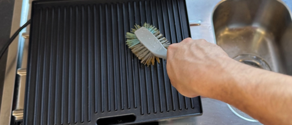 Eine Person reinigt mit einer Bürste die Grillfläche des getesteten Tefal-Kontaktgrills.