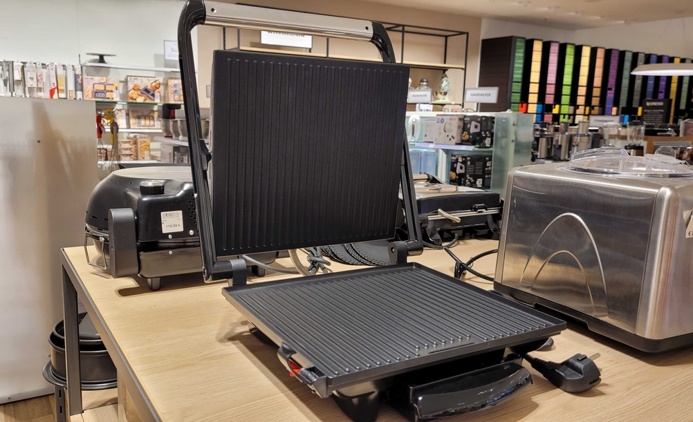 Ein Kontaktgrill steht aufgeklappt auf einer Fläche zum Testen.