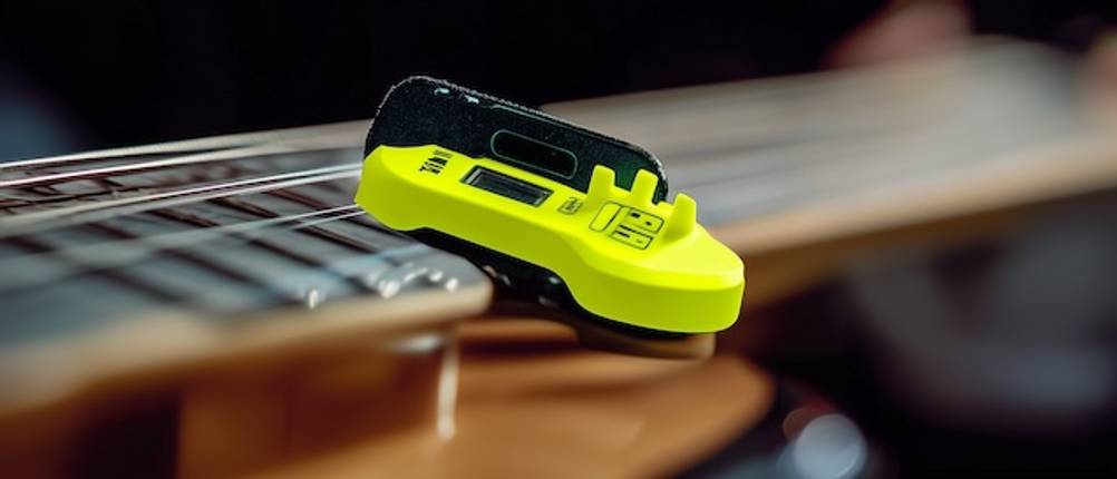 Stimmgerät mit der Konzertgitarre getestet: Nahaufnahme eines gelben Clip-On-Stimmgerätes auf dem Griffbrett einer Gitarre.