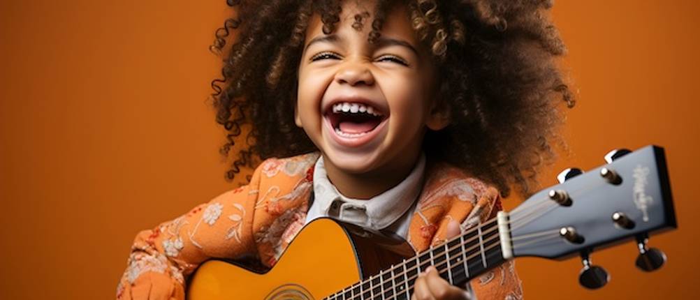 Konzertgitarre von Kind getestet: Ein Kind mit braunen Locken hält lachend eine Gitarre in seiner Hand.