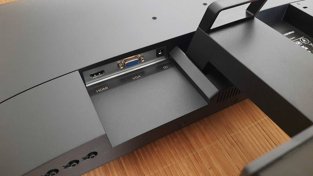 Detailansicht der Anschluss-Buchsen auf der Rückseite des schwarzen Bildschirms eines Koorui 24-Zoll-Monitors im Test, der auf einer hellbraunen Bastmatte liegt.