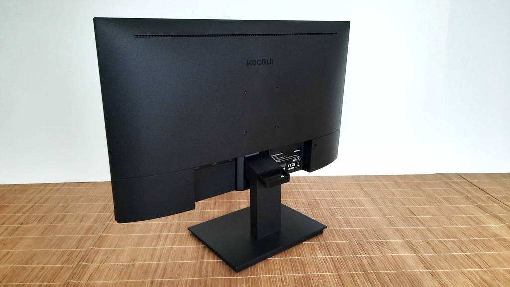 Ansicht von hinten Ansicht auf eines schwarzen Koorui 24-Zoll-Monitor im Test, der sich inklusive Standfuß auf einer hellbraunen Bastmatte steht.