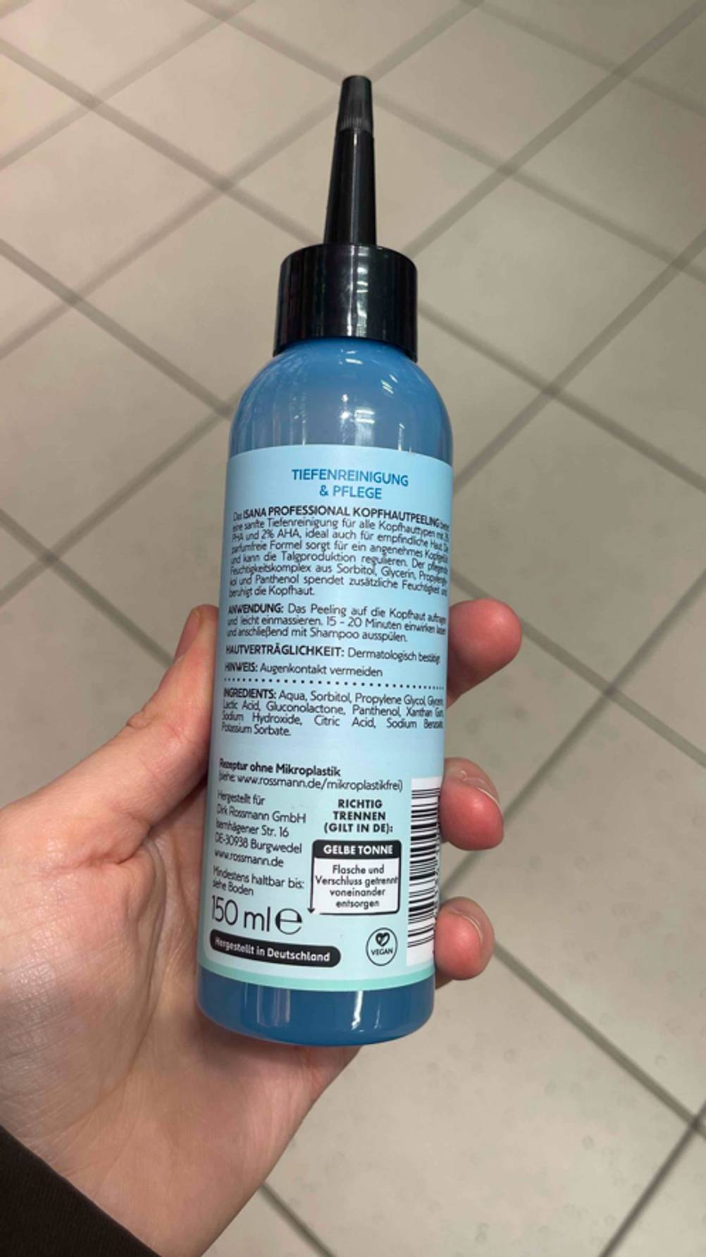 Eine Hand hält die Flasche des Kopfhaut-Peeling im Test mit der Rückseite nach vorne.
