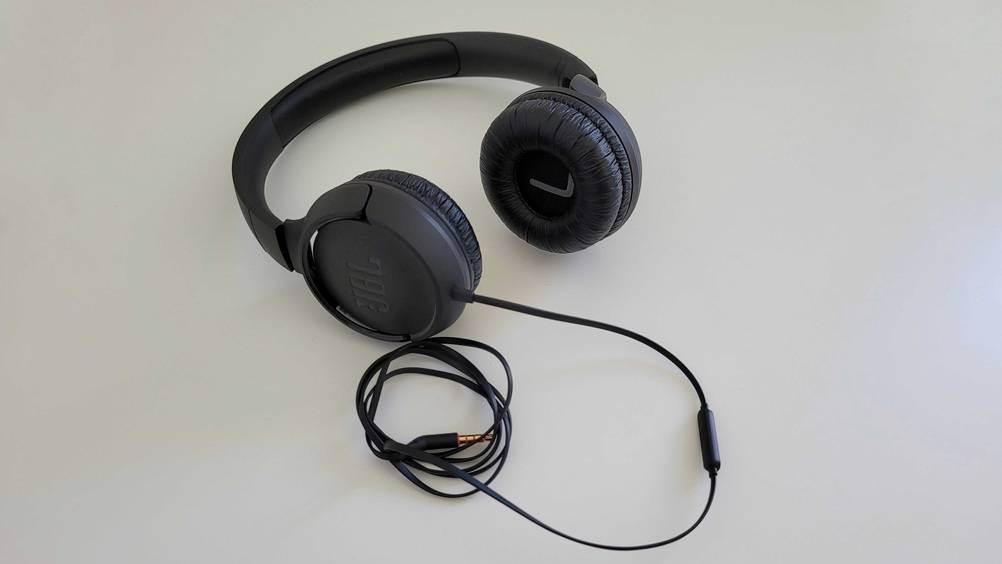 Die getesteten Kopfhörer mit aufgerolltem Kabel davor auf einer hellen Fläche.