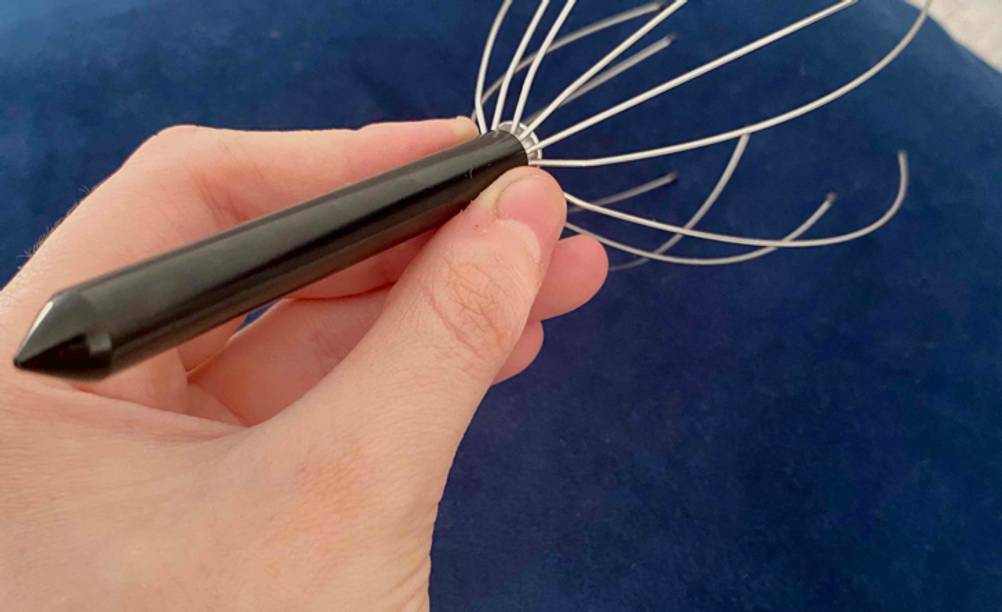 Eine Hand hält den Griff einer getesteten Kopfmassage-Spinne.