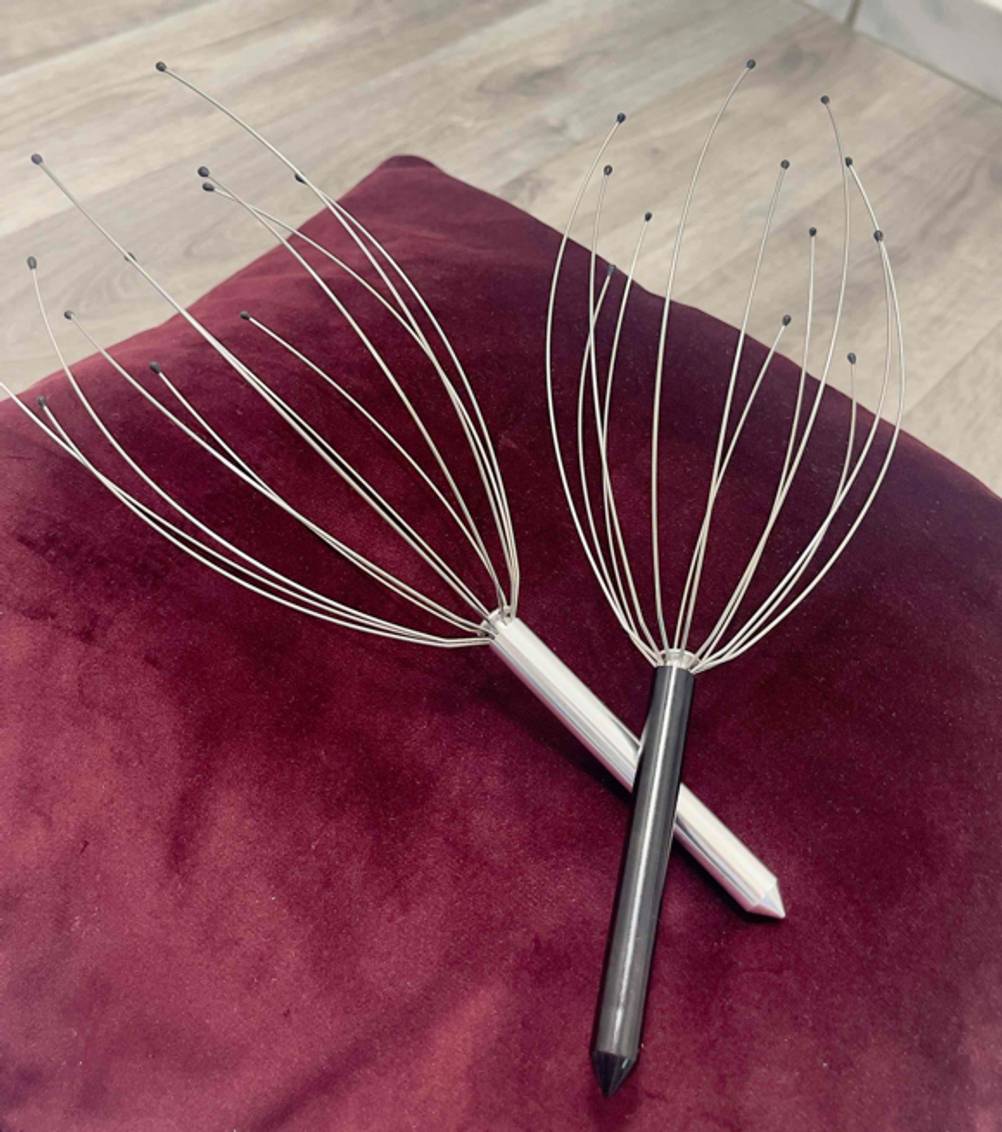Zwei Kopfmassage-Spinnen liegen über Kreuz zum testen auf einem roten Tuch.