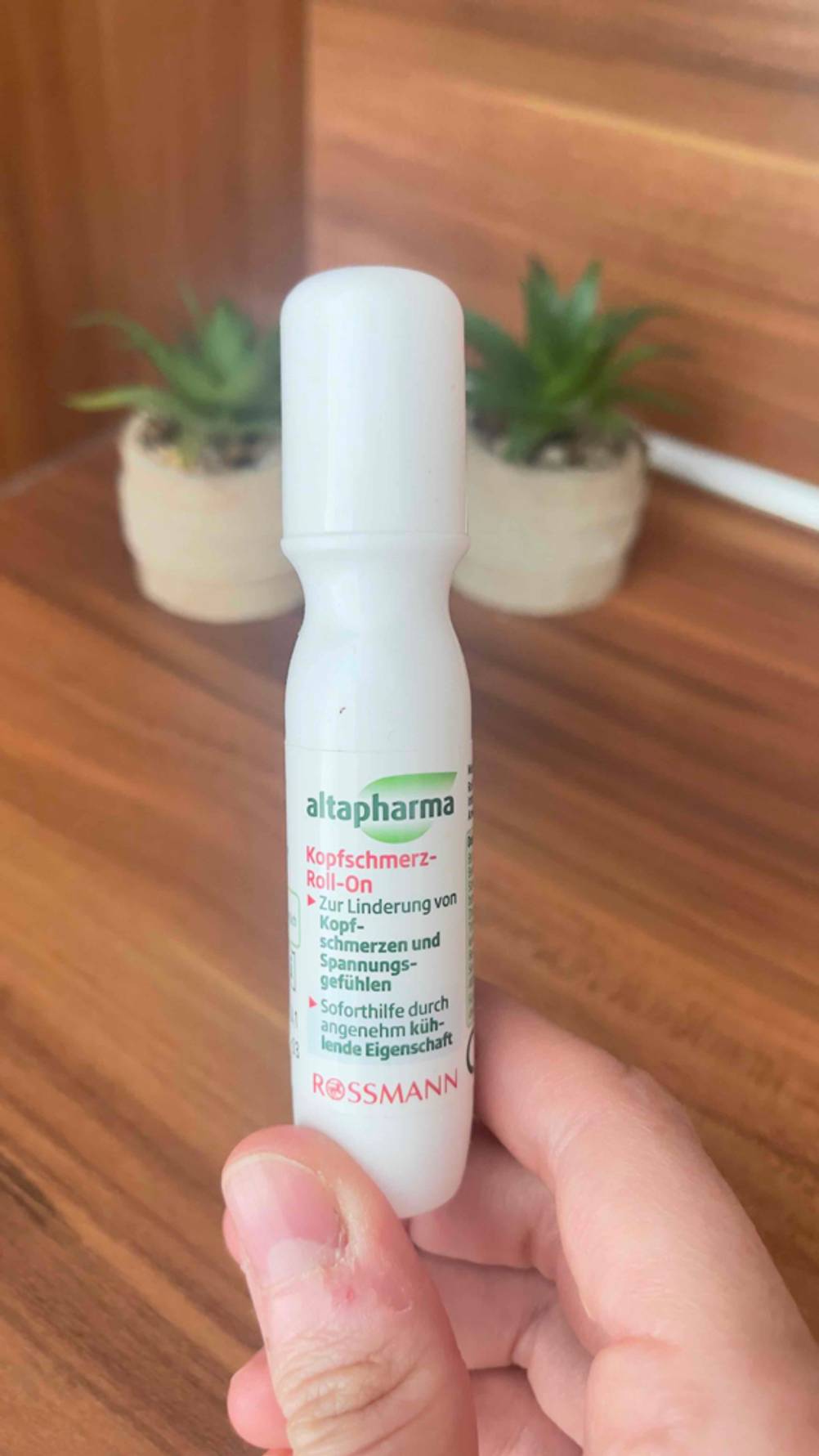 Test: Eine Hand hält den Kopfschmerz-Roll-on vor eine Holzfläche.