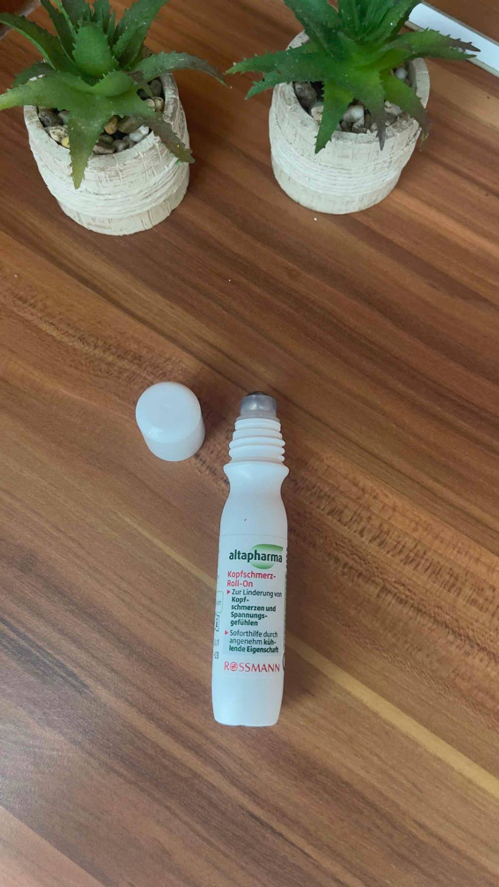 Der getestete Kopfschmerz-Roll-on liegt auf einer Holzfläche vor Pflanzen mit der Kappe daneben.