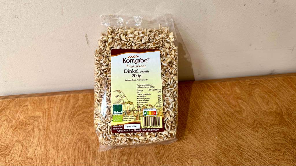 Eine transparente Tüte mit gepufftem Dinkel im Test steht vor einer weißen Wand.