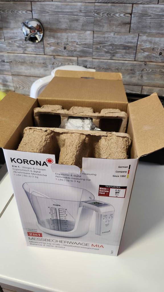 Eine geöffnete Verpackung inklusive eines getesteten Messbechers mit Waage im Test steht auf einer Küchenarbeitsplatte.