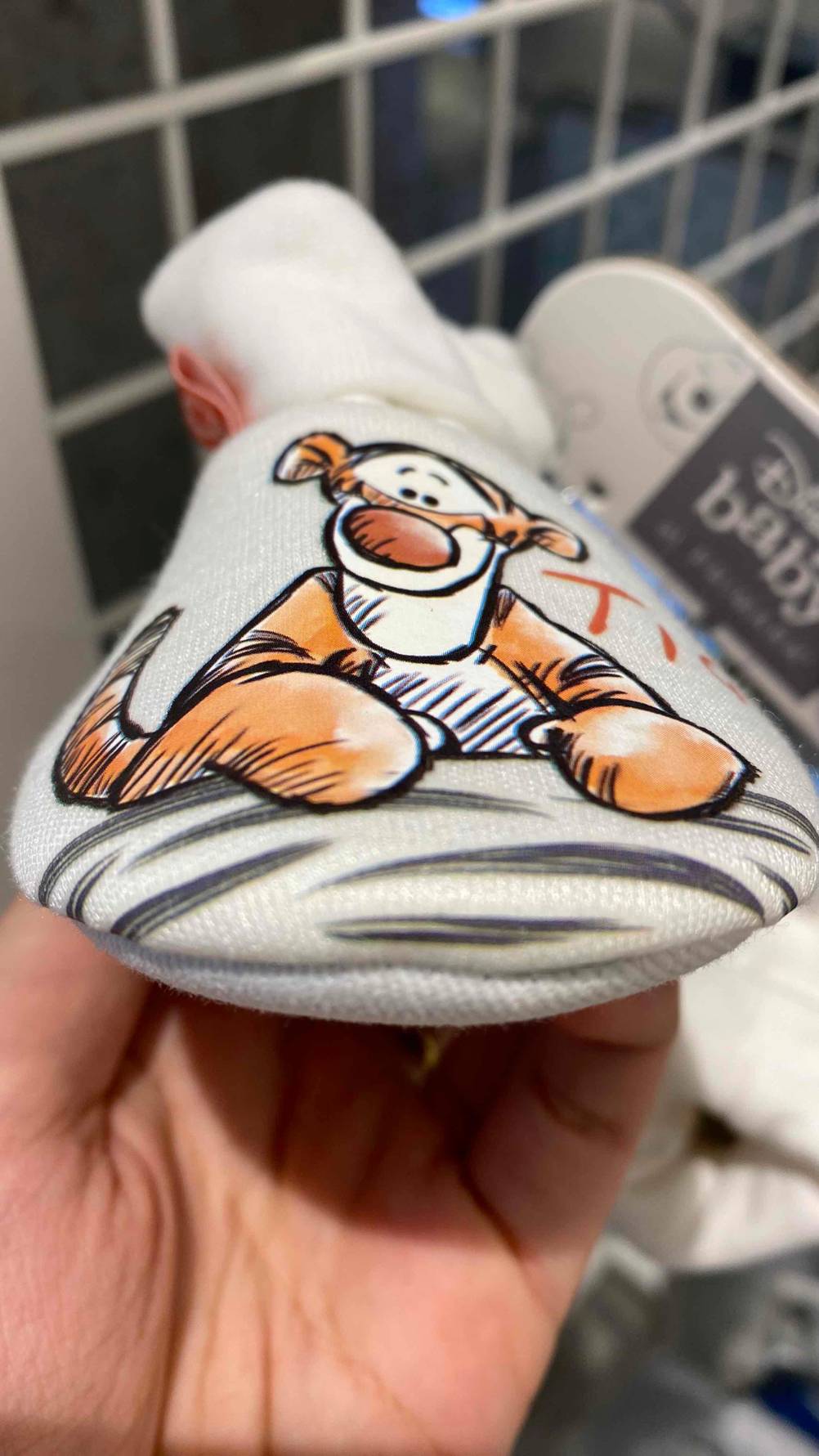 In einer Hand befinden sich getestete Krabbelschuhe für Jungen mit Tiger-Motiv. 