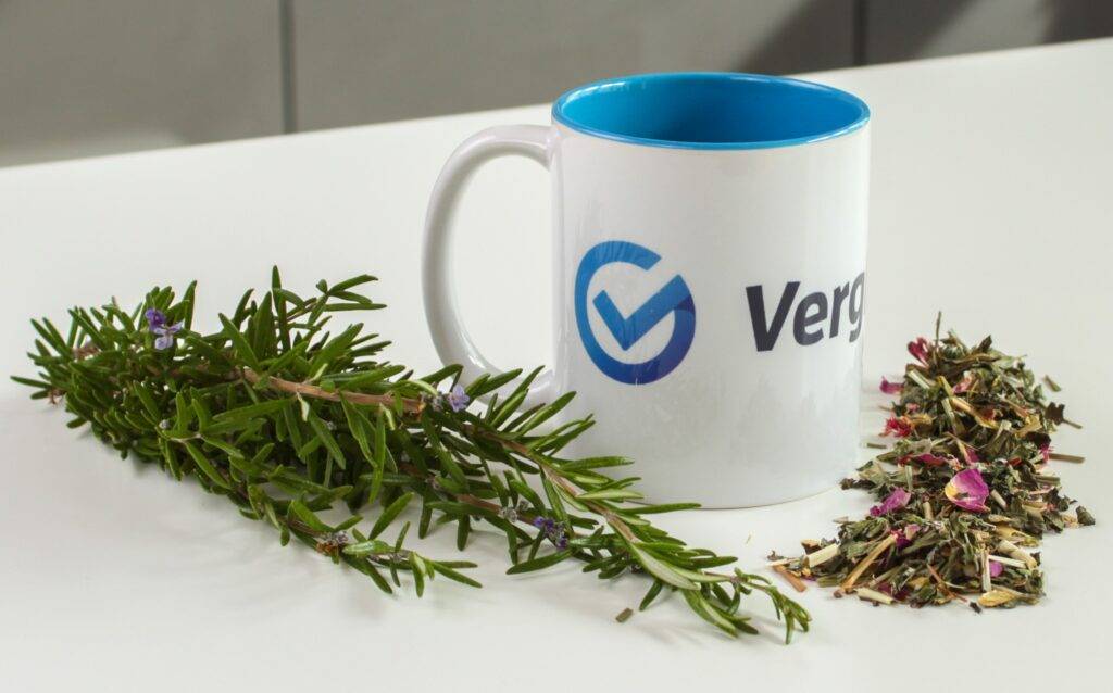 Kräutertee-Test: Eine vergleich-org-Tasse steht auf einem weißen Tisch inmitten von Kräutern.