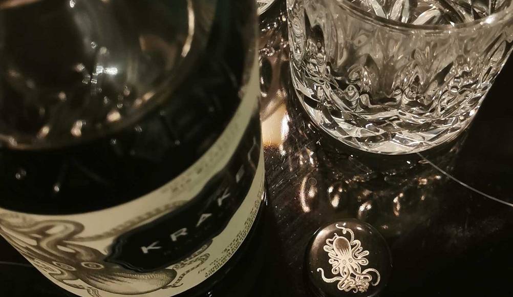 Rum im Test: Ansicht von oben auf eine Flasche Rum neben zwei Kristallgläsern auf dunkler Oberfläche.