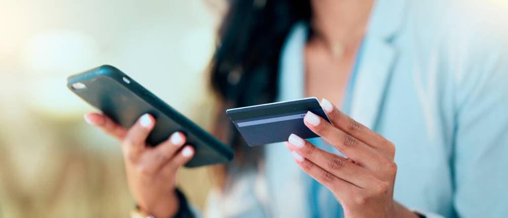 Kreditkarten getestet: Eine Frau hält ein Smartphone und eine Kreditkarte in den Händen.