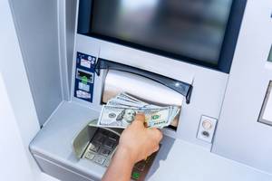 Test der Kreditkarten: Eine Hand nimmt mehrere Dollar-Scheine aus einem Geldautomaten.