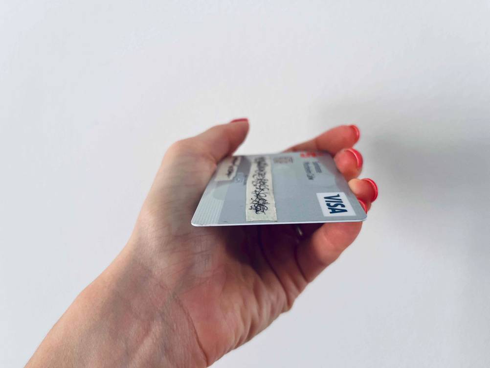 Eine Hand hält eine Kreditkarte im Test flach vor eine helle Wand.