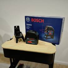 Der Kreuzlinienlaser von Bosch steht neben seiner Verpackung auf einem Rollwagen.